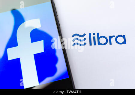 Facebook Libra. FB logo sulla schermata dello smartphone con un pollice in alto l'ombra e la brochure con il logo di libra. A titolo illustrativo per notizie su Libra cryptocurrency. Foto Stock