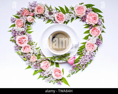 Cornice di fiori a forma di cuore: rosa, lilla, rowan foglie e tazza di caffè su uno sfondo bianco. Motivo floreale. Foto Stock
