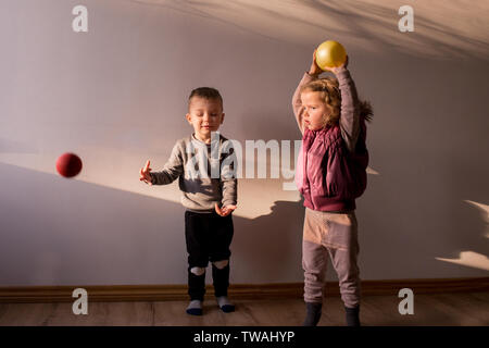 Due bambini che giocano al suo interno, in una stanza soleggiata, con po' di palline rimbalzanti, gettarli in aria Foto Stock