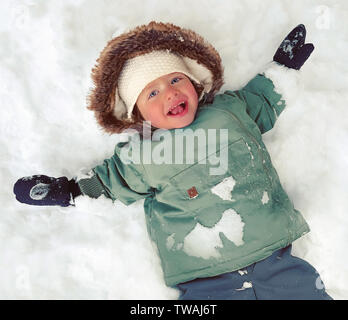 Sorridono felici, grazioso bambino con gli occhi blu godendo di inverno e rendendo angelo di neve Foto Stock