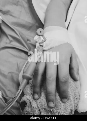 Foto in bianco e nero con la mano di un malato bambina in un ospedale pediatrico di riserva, con una cannula e tenendo un orsacchiotto Foto Stock