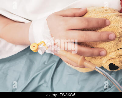 Dettagli con la mano di un malato bambina in un ospedale pediatrico di riserva, con una cannula e tenendo un orsacchiotto Foto Stock