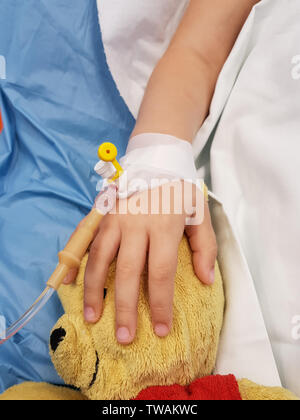 Dettagli con la mano di un malato bambina in un ospedale pediatrico di riserva, con una cannula e tenendo un orsacchiotto Foto Stock