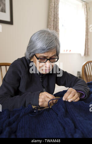 Una vecchia donna indiana di etnia asiatica maglia in un inglese home Foto Stock