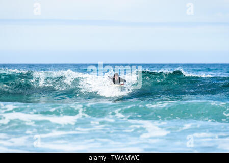 Surfer uomo con la tavola da surf è pagaiando sull'onda. Guy nel surf muta è la remata le ondate di freddo oceano atlantico in Galizia, Spagna. Foto Stock