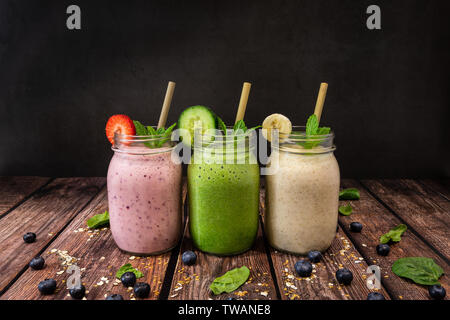 Deliziosi cibi organici banana, fragola e cetriolo, lino e chia seme frullati di frutta shot sul tavolo di legno contro un nero ardesia sfondo. Inoltre pict Foto Stock