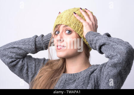 Ritratto di giovane carina ragazza fiducioso cercando su giallo cappuccio di maglia per il freddo inverno su sfondo grigio chiaro. Foto Stock