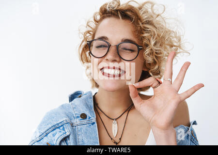 Close-up shot di rilassati e felici entusiasta amichevole-cercando unbothered ragazza con breve taglio di capelli ricci e forato naso con gli occhiali occhiolino Foto Stock