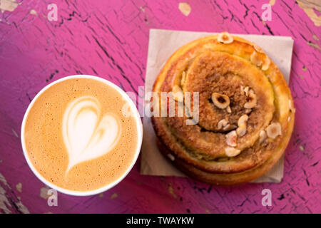 Il Cappuccino e cannella rotolo di pasta isolati su peeling e incrinato rosa legno dipinto dal di sopra. Foto Stock