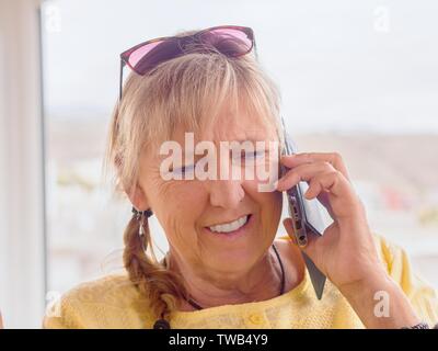Ritratto di una donna di mezza età. Lei è al telefono con il Movil telefono, ha avuto capelli biondi, occhiali da sole sulla sua testa, una treccia treccia sul suo lato. B Foto Stock