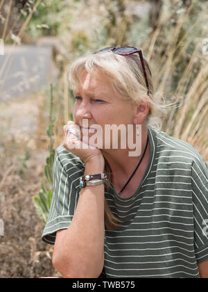 Ritratto di una donna nella natura, con erbe in background. Naturale, morbido carisma, positivo, leggermente espressione pensosa, capelli biondi, cantata Foto Stock