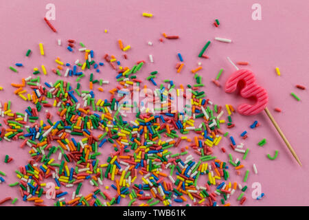 Compleanno sfondo con multi-colore di torta topping spruzza e numero 3 compleanno candela su sfondo rosa - vista superiore Foto Stock