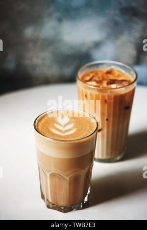 Il latte e il ghiaccio latte nel caffè bicchieri sul tavolo bianco in cafe. A caldo e a freddo il concetto di bevanda. Foto Stock