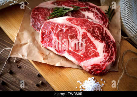 Due materie costata di manzo su una tavola di legno su un tavolo preparato per il grill. Vista dall'alto in stile rustico Foto Stock