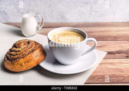 Colazione perfetta di una casalinga bun cannella, caffè e bicchiere di latte caraffa sul tavolo di legno. Stile rustico. Close-up. Foto Stock