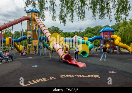 I genitori e i bambini in un momento di relax a le diapositive in un parco giochi aree di Lumea Parcul Copiilor, il mondo bambini parco nel centro di Bucarest, Romania. Foto Stock