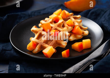 Cialde belghe con persimmon sulla piastra nera in stato d'animo scuro stile - close up fotografia orizzontale di fresche dolci cotti al forno con dessert arance mature exoti Foto Stock