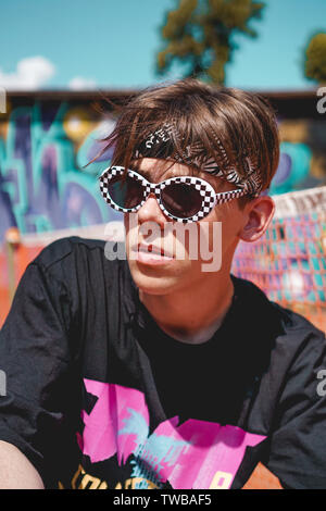Ritratto di un giovane uomo con occhiali da sole rilassante contro lo sfondo di graffiti esterni Foto Stock