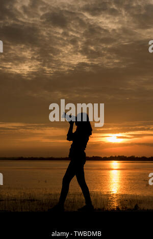 Silhouette bello fotografo scatta una foto con la fotocamera professionale sul tramonto. Foto Stock