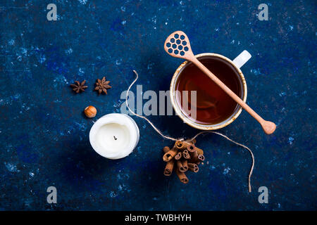 Autunno tazza di tè con un cucchiaio di miele, una candela, cannella e anice stellato su uno sfondo blu scuro. In autunno il layout, vista dall'alto, laici piatta Foto Stock