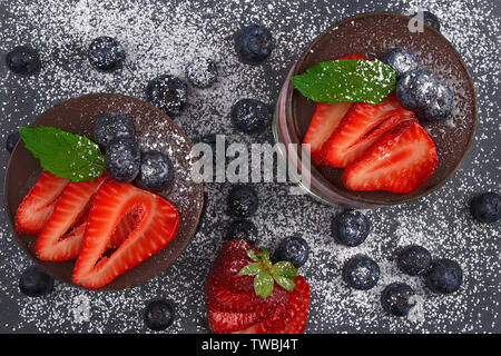 Mousse di ciliegio con biscotti sbriciolati, ciliegie sciroppate, ananas panna e cioccolato. Decorate con fragole, mirtilli e foglie di menta Foto Stock