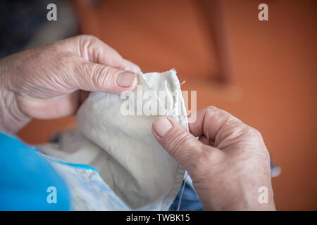 Una donna anziana cuce abiti strappati. close-up di le mani delle donne con il filo e l'ago. il concetto di povertà. Foto Stock