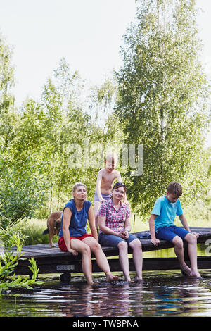 Famiglia di trascorrere del tempo insieme seduti su un ponte su un lago, tra gli alberi, vicino alla natura, durante le vacanze estive. Candide persone, momenti di vero e proprio, Foto Stock