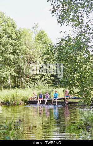 Famiglia di trascorrere del tempo insieme seduti su un ponte su un lago, tra gli alberi, vicino alla natura, durante le vacanze estive. Candide persone, momenti di vero e proprio, Foto Stock