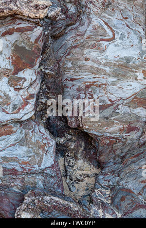 Cove nella roccia con sabbia lasciata dalle onde del mare e dove le diverse tonalità di colore della roccia formano un disegno astratto. Foto Stock