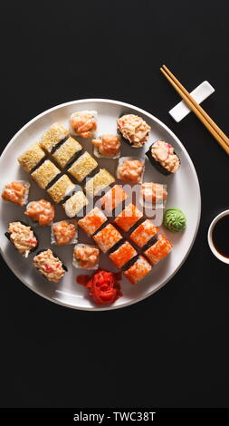 Sushi fatti a mano e i rulli sulla piastra bianca con bacchette di legno su sfondo nero, panorama verticale Foto Stock
