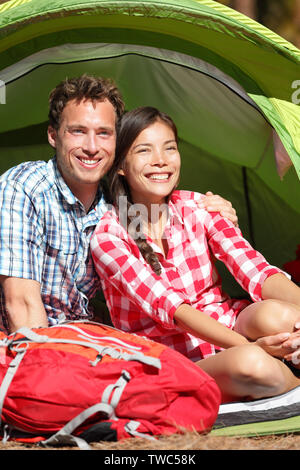 Matura in Campeggio in tenda felice nel romanticismo sorridendo felice all'aperto nella foresta e godere di amore guardando a vista. Felice interracial matura per rilassarsi dopo le attività outdoor escursionismo. Donna asiatica, uomo caucasico. Foto Stock