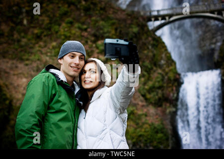 Coppia giovane tenendo fotografare accanto a cascata Foto Stock