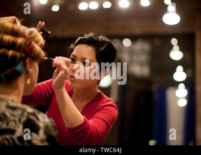 Make up Artist di applicare il make-up per donna con bigodini in i suoi capelli. Foto Stock