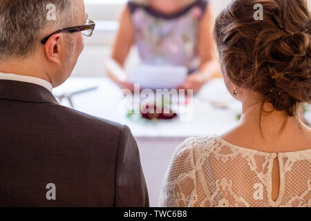 Scenario di nozze: giovane partecipa alla cerimonia di nozze con la femmina ceremnony master a leggere i giornali con gli anelli di nozze sulla tavola. Foto Stock
