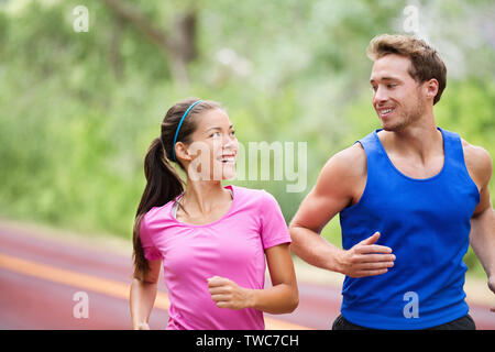 Uno stile di vita sano - Esecuzione di coppia fitness jogging ridendo, parlando al di fuori sulla strada nella splendida natura. Multirazziale sport giovane, donna asiatica modello e uomo modello fitness esercizio sorridendo felice. Foto Stock