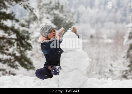 Carino bambina fa un pupazzo di neve in inverno parco innevato. Foto Stock