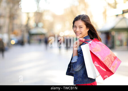 Donna shopping - shopper all'aperto ragazza sorride felice azienda borse per lo shopping. Ritratto di donna shopper guardando la fotocamera su strada a piedi La Rambla, Barcelona, Spagna. Razza mista donna asiatica. Foto Stock