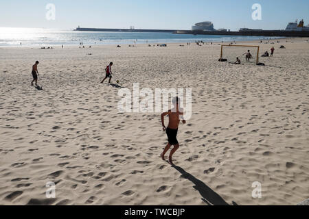 I giovani che giocano a calcio sulla spiaggia di sole primaverile Matosinhos e la vista del porto di Leixões & Cruise Terminal Porto Portogallo Europa KATHY DEWITT Foto Stock