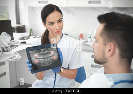 Dentista femmina mostra denti x-ray su tavoletta digitale sullo schermo. Paziente seduto su una sedia in professional dental clinic. Foto Stock