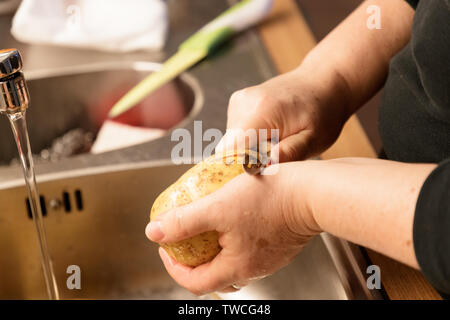 La donna la pelatura di patate sopra un lavandino closeup Foto Stock