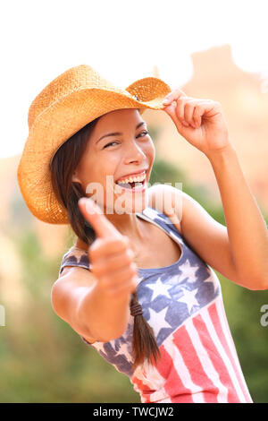 American cowgirl donna felice eccitato dando Thumbs up indossando il cappello da cowboy in esterno e in campagna. Allegro euforico gioiosa donna sorridente godendo della libertà. Bella multirazziale caucasico asiatici femmina. Foto Stock
