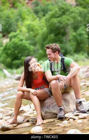 Escursionismo persone - escursionista giovane felice nel Parco Nazionale di Zion parlando e il riposo. Giovane donna e uomo escursionista seduta dal fiume di acqua creek godendo di vista sorridente. Coppia giovane per rilassarsi dopo le escursioni, Utah, Stati Uniti d'America. Foto Stock