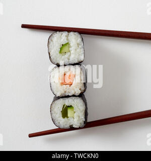 Alimentare il concetto di styling con tre maki sushi rotoli con nori alghe, salmone e avocado pera posto tra le bacchette di bambù su bianco con spazio di copia Foto Stock