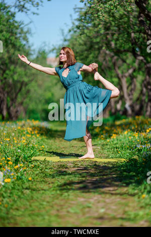 Foto di giovane donna in lungo abito verde facendo yoga in foresta Foto Stock