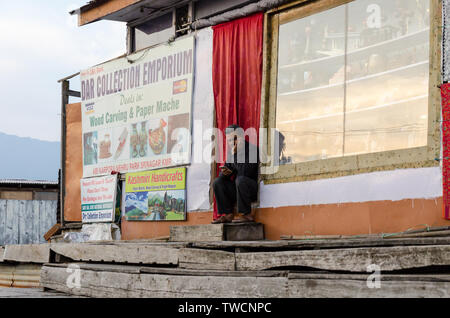 Negoziante seduta all'ingresso del suo negozio su dal lago, Srinagar, Jammu e Kashmir India Foto Stock