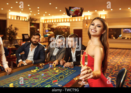 Una giovane donna bionda con un bicchiere di champagne in un abito al tavolo della roulette giocando a poker in un casinò. Foto Stock