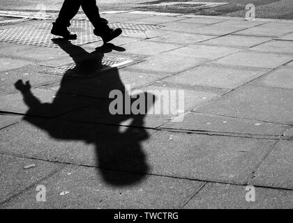 Pavimentazione in ombra di una persona utilizzando un telefono cellulare. astratta. Foto Stock