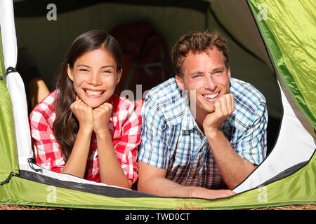 Felice coppia romantica in Campeggio in tenda cercando nella foresta. Camper sorridendo felice all'aperto nella foresta rilassante. Multirazziale giovane avendo divertimento rilassante dopo l'attività all'aperto. Donna asiatica, uomo caucasico. Foto Stock