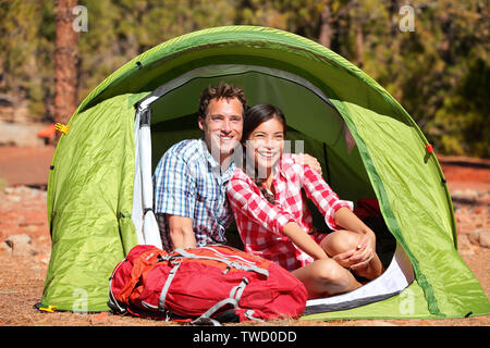 Matura in Campeggio in tenda felice nel romanticismo sorridendo felice all'aperto nella foresta e godere di amore guardando a vista. Felice interracial matura per rilassarsi dopo le attività outdoor escursionismo. Donna asiatica, uomo caucasico. Foto Stock