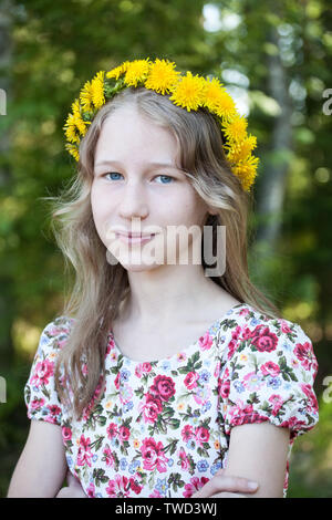 Ragazza giovane nella corona di tarassaco ritratto su alberi verdi sfondo sfocato Foto Stock